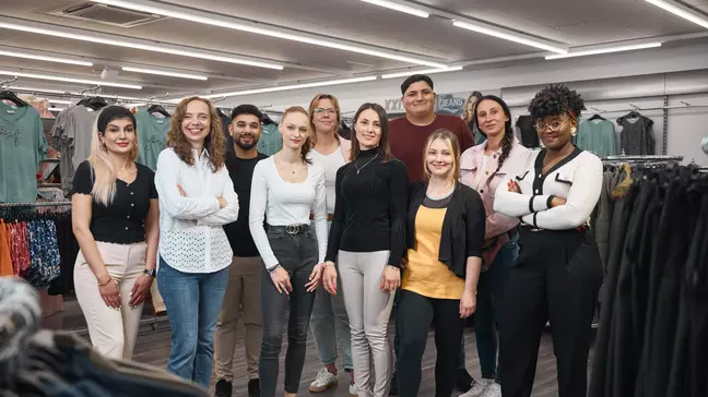 Een groep medewerkers staat samen in een filiaal voor kledingrekken en kijkt naar de camera.