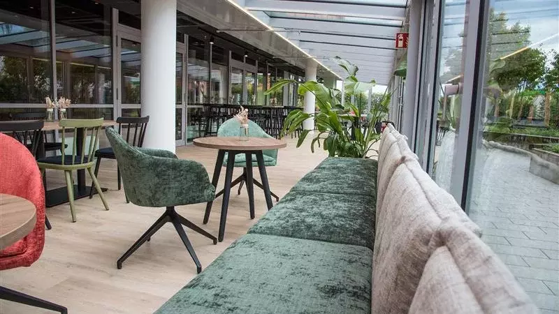 Binnenaanzicht van een moderne kantine met zitplaatsen bij het raam, tafels, stoelen en planten.