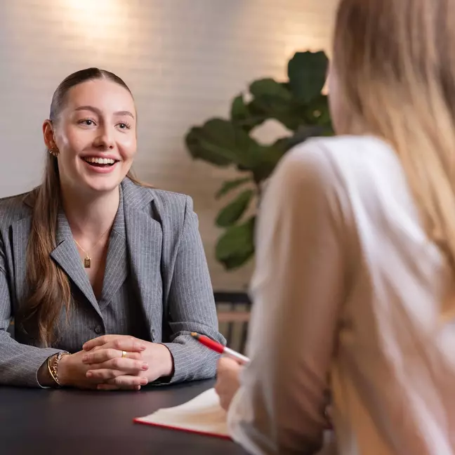 Een medewerkster praat glimlachend met een andere medewerkster aan een tafel in een kamer