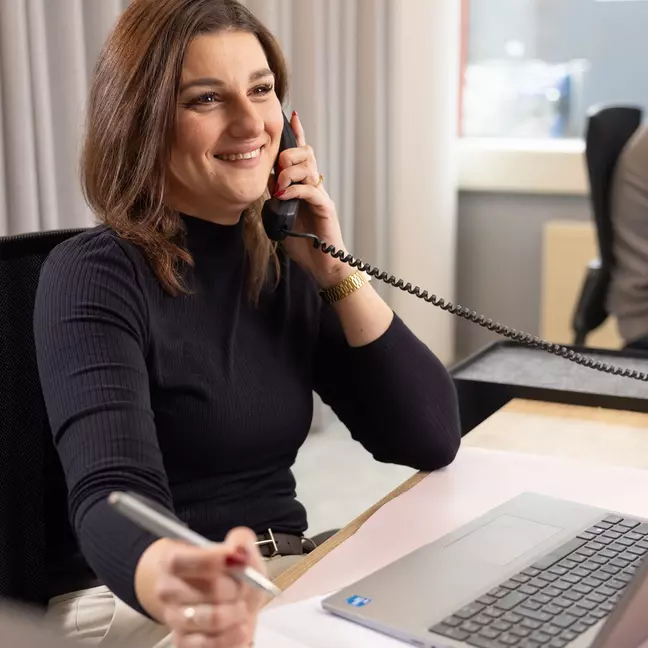een vrouw zit op haar werk te bellen en glimlacht