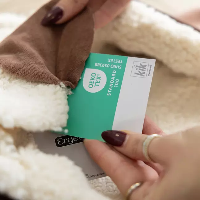 Iemand bekijkt de voering van een kledingstuk en houdt daarbij een OEKO-TEX® Standard 100-keurmerk met het KiK-logo in de hand