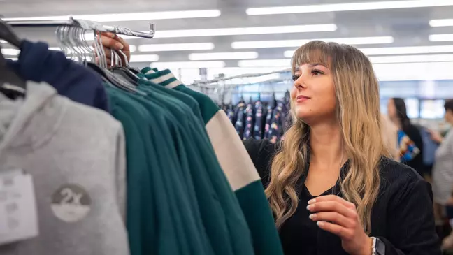 Een jonge medewerkster sorteert sweatshirts op een kledingrek