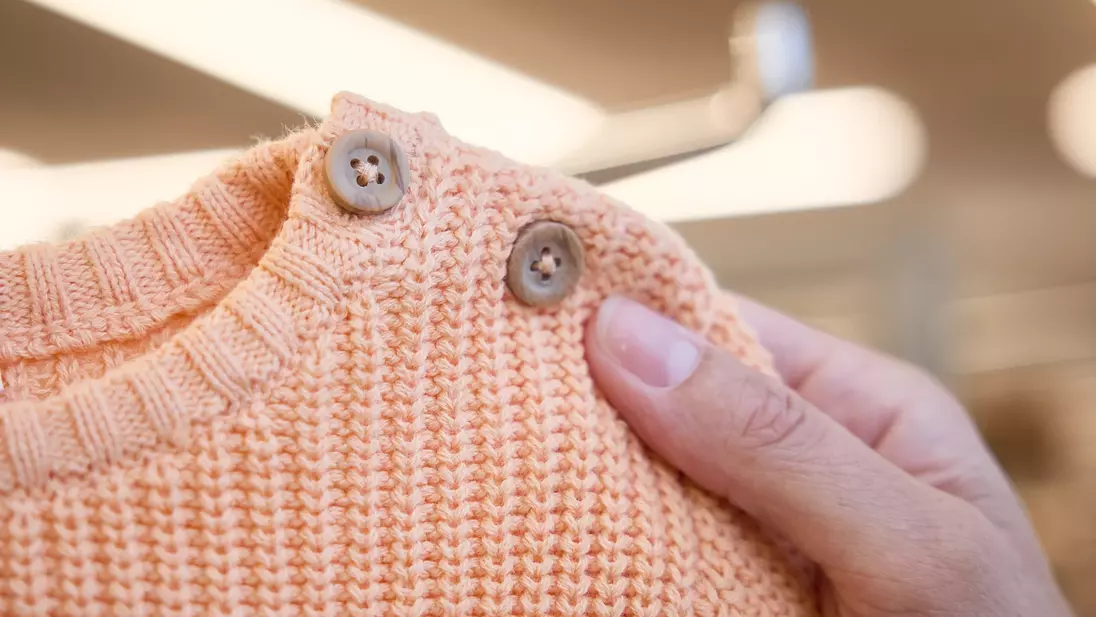 Een hand houdt een oranje kindertrui vast met knoopjes bij de hals