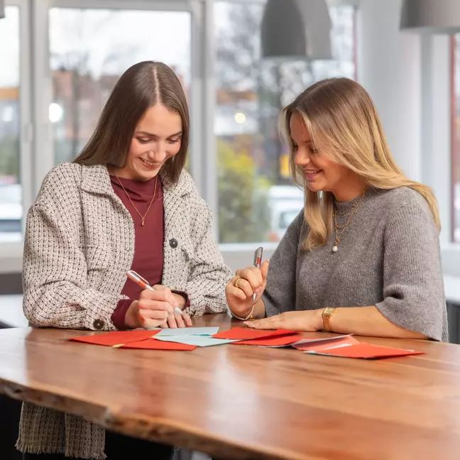 Twee medewerksters werken samen aan documenten in een moderne vergaderruimte.