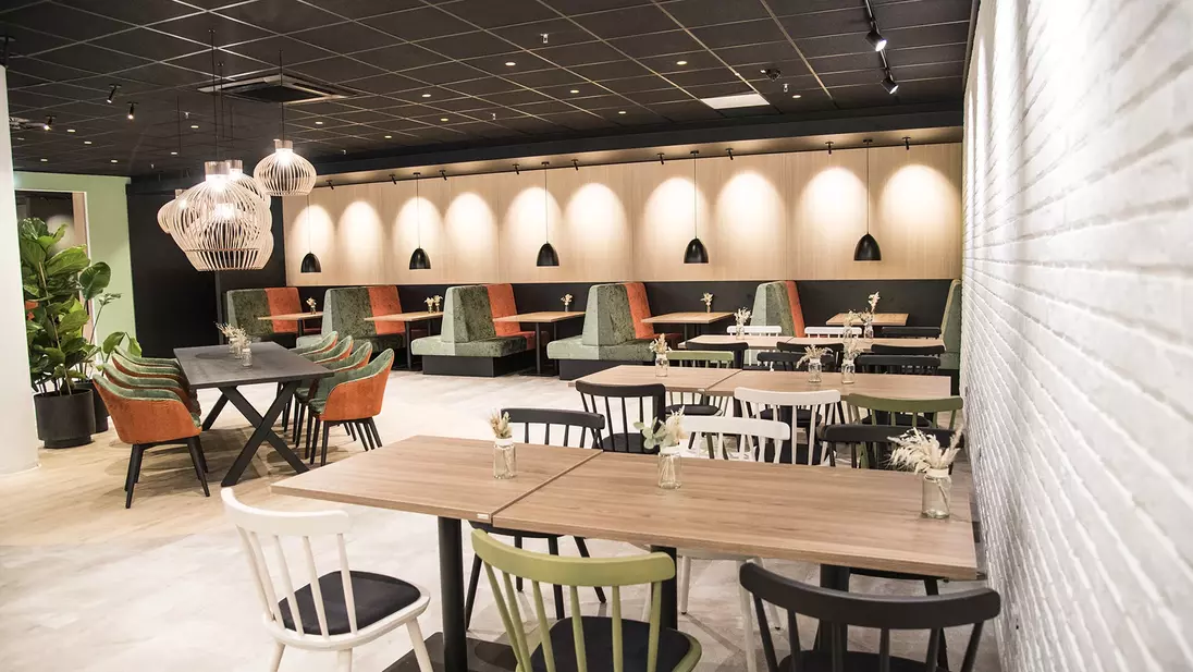 Binnenaanzicht van een modern ingerichte kantine met tafels, stoelen en zitnissen.