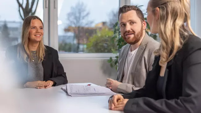 Twee jonge vrouwen en een jonge man zitten aan een tafel en praten met elkaar