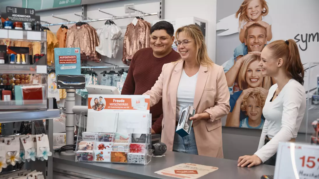 Drie mensen staan samen bij een toonbank in een winkel en kijken naar de kassa.